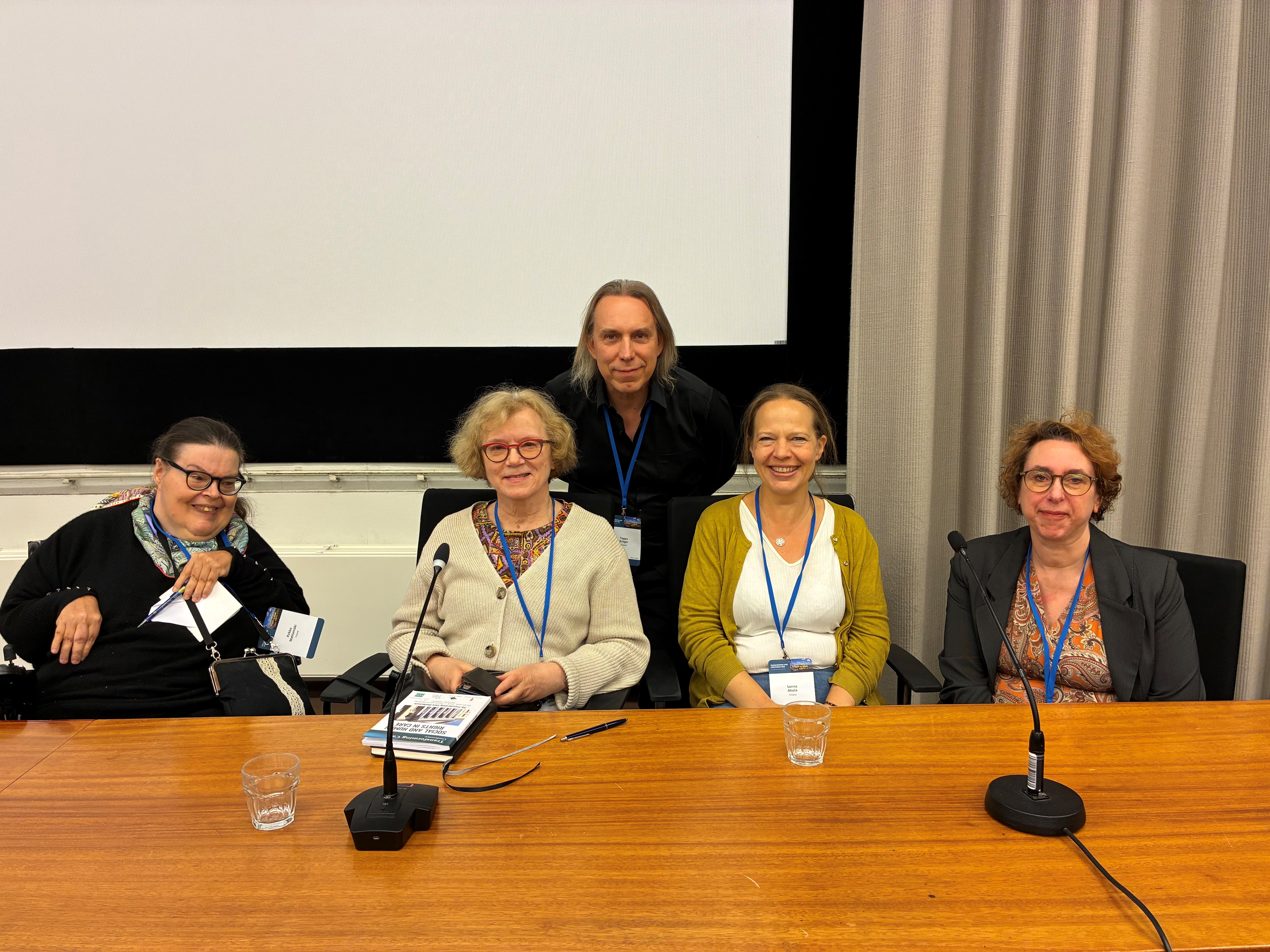 Ryhmäkuva, jossa pöydän takana vasemmalta oikealle Pirkko Mahlamäki, Marja Jylhä, Teppo Kröger, Sanna Ahola ja Kirstein Rummery.